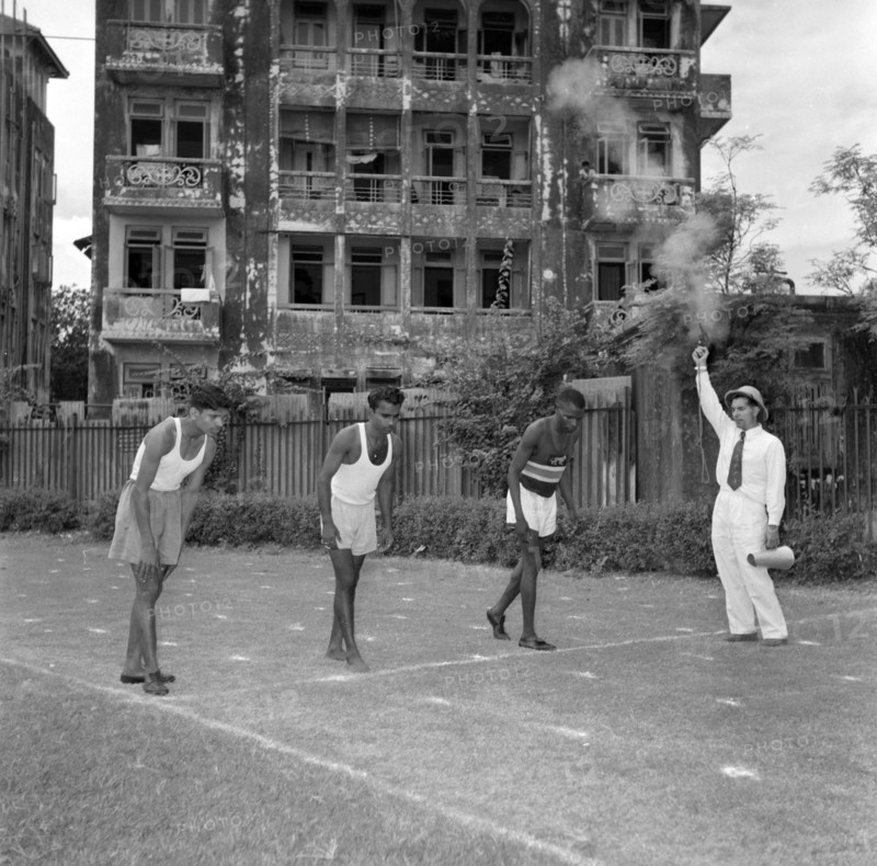 On the starting blocks. A starting pistol fires for three Olympic athletes on the starting line of a practice race. India, 2 November 1956. India, Southern Asia, Asia.