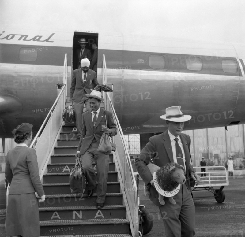Athletes arrive in Australia. Athletes in the 1956 Kenyan Olympic team descend the steps of an aeroplane on their arrival in Australia. One man clutches the team's mascot, a lion, under his arm. Australia, 4 November 1956. Australia, Australia, Oceania.