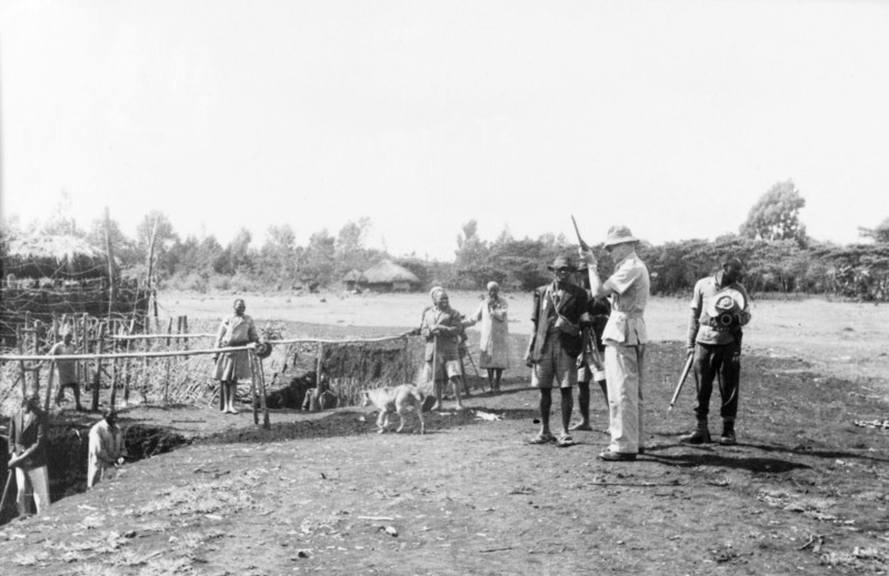 Home Guards at a Kikuyu security village. Armed Kikuyu Home Guards wait for a European man to load his rifle at a fortified security village. To the left, Kikuyu men can be seen digging a moat to provide further protection against Mau Mau attack. Kenya, circa 1955. Kenya, Eastern Africa, Africa.
