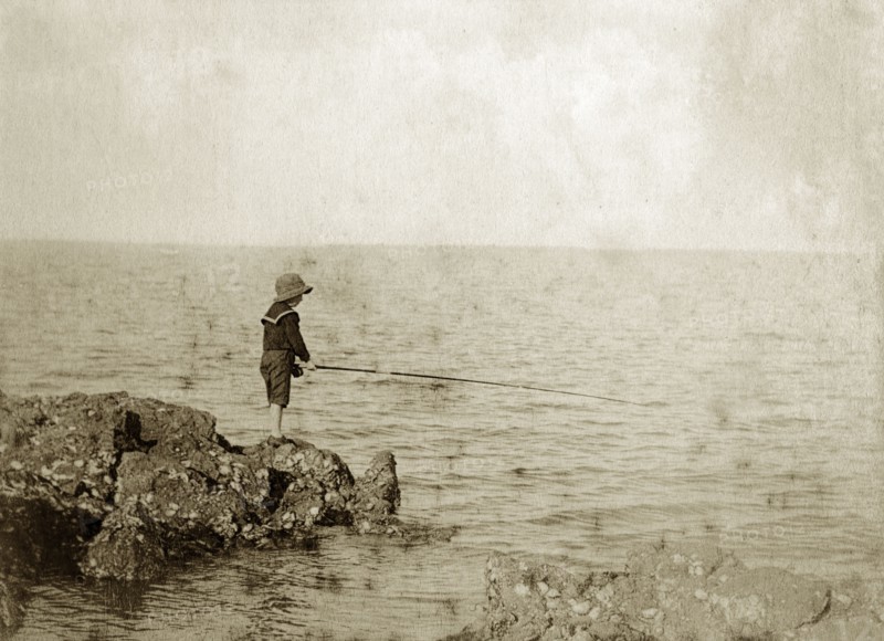 Young boy fishing, Australia. A lone boy wearing a sailor suit and hat, holds his fishing line out over rocks into the sea in the hope of catching a bite. Queensland, Australia, circa 1890., Queensland, Australia, Australia, Oceania.