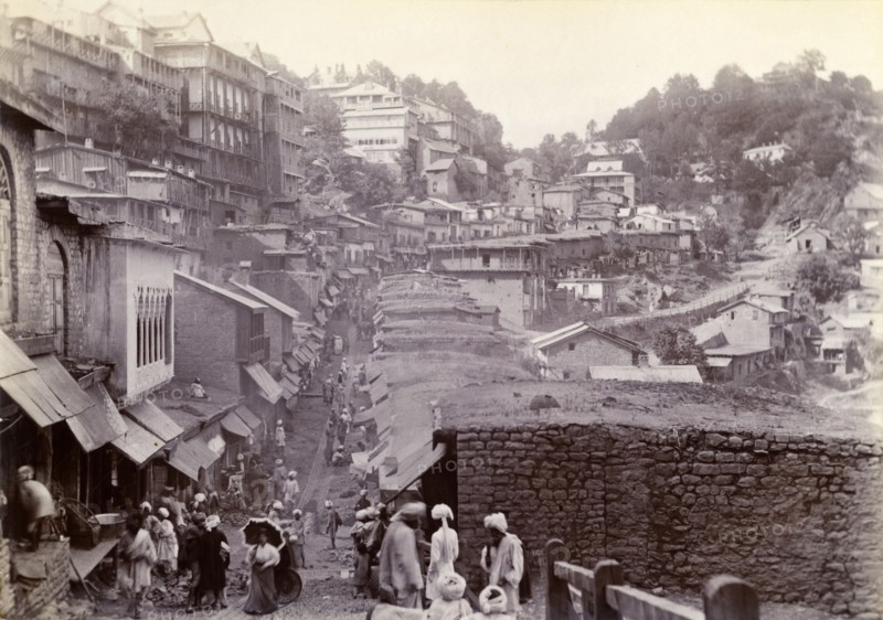 Bustling market street at Murree. Shop awnings line a bustling market street that winds down from the hills into the town of Murree. A lone British women holding a parasol can be see amongst the crowds of Pakistani locals. Murree, Punjab, India (Punjab, Pakistan), circa 1895. Murree, Punjab, Pakistan, Southern Asia, Asia.
