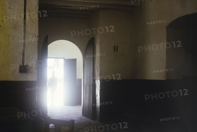 Interior of slave market, Elmina Castle. A sunlit doorway leads into the dark interior of the old slave market at Elmina Castle. An original caption tells us that 'slaves were viewed by buyers through squint holes' in this room. Ghana, circa 1965. Elmina, Central (Ghana), Ghana, Western Africa, Africa.