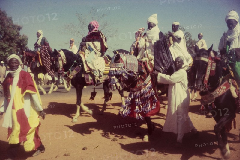Decorated horses, Nigeria. Men dressed in ceremonial attire ride horses decorated with tassles and ornate bridles at a procession marking the end of Ramadan. Zaria, Nigeria, 1958. Zaria, Kaduna, Nigeria, Western Africa, Africa.