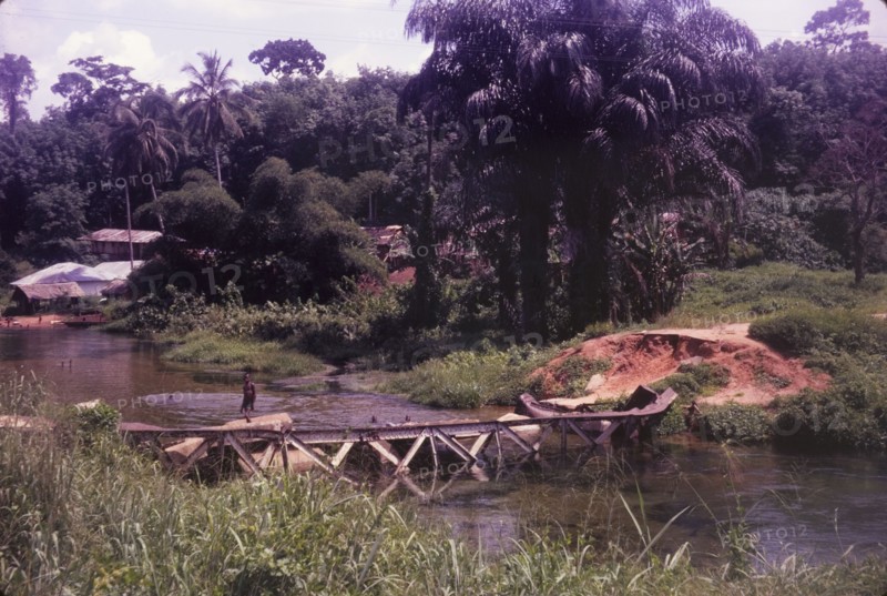 Collapsed bridge near Ore. The twisted girders of a collapsed bridge near Ore lie semi-submerged in a river. The bridge was demolished in raids carried out during the Nigerian Civil War (1967-70). Near Ore, Lagos, Nigeria, circa 1970., Lagos, Nigeria, Western Africa, Africa.