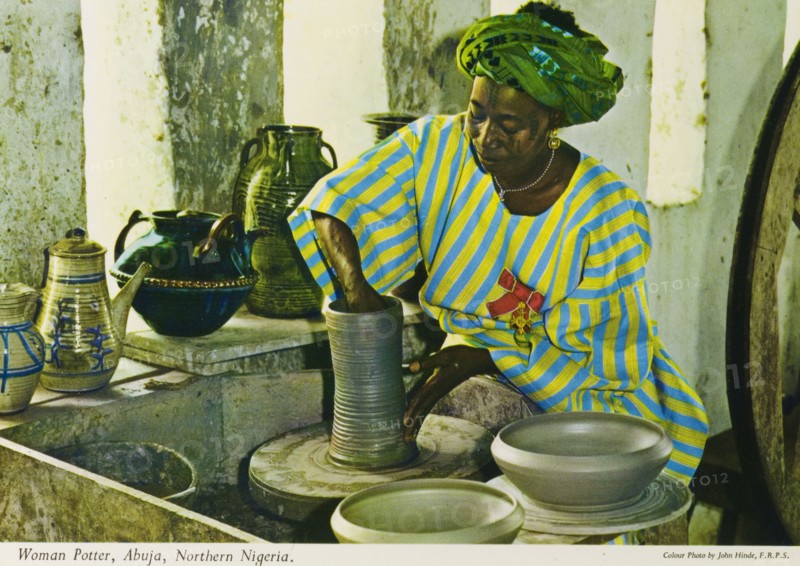 Potter's studio, Nigeria. A colourful tourist postcard depicts a Nigerian craftswoman working on a clay vase at a potter's wheel. A selection of finished, glazed pots sits on the windowsill of her studio. Abuja, Nigeria, circa 1975. Abuja, Abuja, Nigeria, Western Africa, Africa.