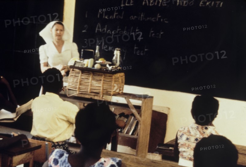 PTS nursing exam. A qualified nurse presides over a Preliminary Training School (PTS) entrance exam, held for nurses training to work at a Church of Nigeria hospital. Notes on the blackboard list three parts of the exam, which include a mental arithmetic test, an adaptability test and a memory test. Nigeria, circa 1963. Nigeria, Western Africa, Africa.