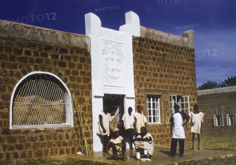 Male patients at a Church of Nigeria hospital. A group of male patients at a Church of Nigeria hospital, loiter outside the entrance to the children's ward. Several wear loosely fitting hospital tunics. Nigeria, circa 1970. Nigeria, Western Africa, Africa.