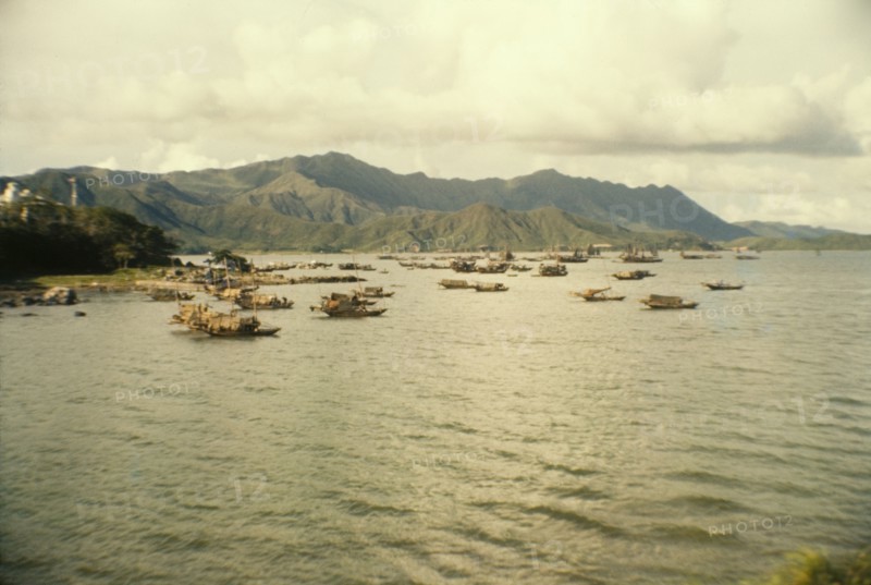 Fishing boats off Tai Po. Mountains form a backdrop to a fleet of Chinese sampans that bob up and down off the coast of Tai Po. Tai Po, Hong Kong, People's Republic of China, July 1960. Tai Po, Hong Kong, China, People's Republic of, Eastern Asia, Asia.