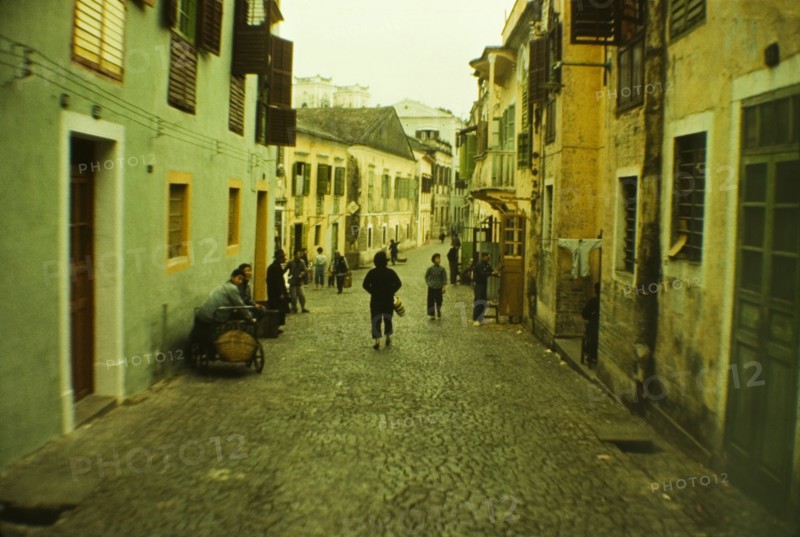 Street scene in Macau. People go about their daily business on a cobbled street bordered by brightly painted houses in the centre of Macau. Macau, People's Republic of China, 2 January 1961. Macau, Macau, China, People's Republic of, Eastern Asia, Asia.