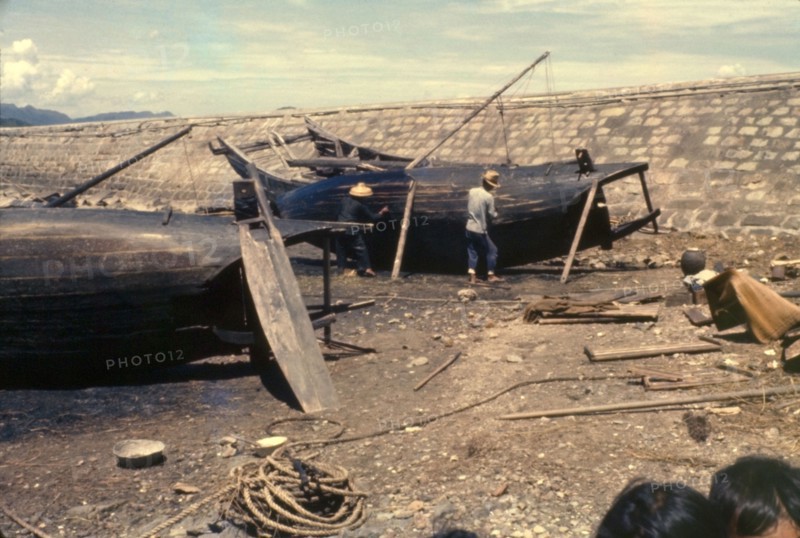 Re-caulking a sampan. Fishermen re-caulk the upturned bottoms of their sampans, filling in the cracks caused by weathering to ensure their vessels are waterproof. Tai Po, Hong Kong, People's Republic of China, August 1960. Tai Po, Hong Kong, China, People's Republic of, Eastern Asia, Asia.