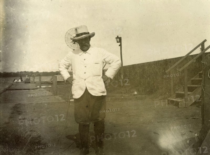 District Commisioner of Entebbe. Portrait of a colonial officer identified as 'James Martin', the District Comissioner of Entebbe, Uganda. He stands, hands on hips, near a jetty on the banks of a river or lake. German East Africa (Tanzania), 1906. Tanzania, Eastern Africa, Africa.