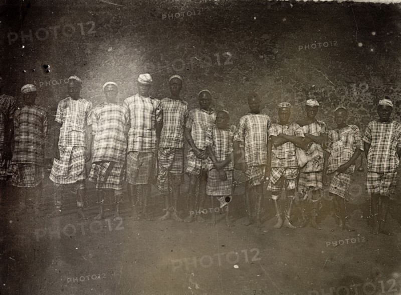 Convicts, Uganda, 1906. Group portrait of men wearing a uniform of checked cloth and ankle chains. A caption identifies them as convicts. Uganda, 1906. Uganda, Eastern Africa, Africa.