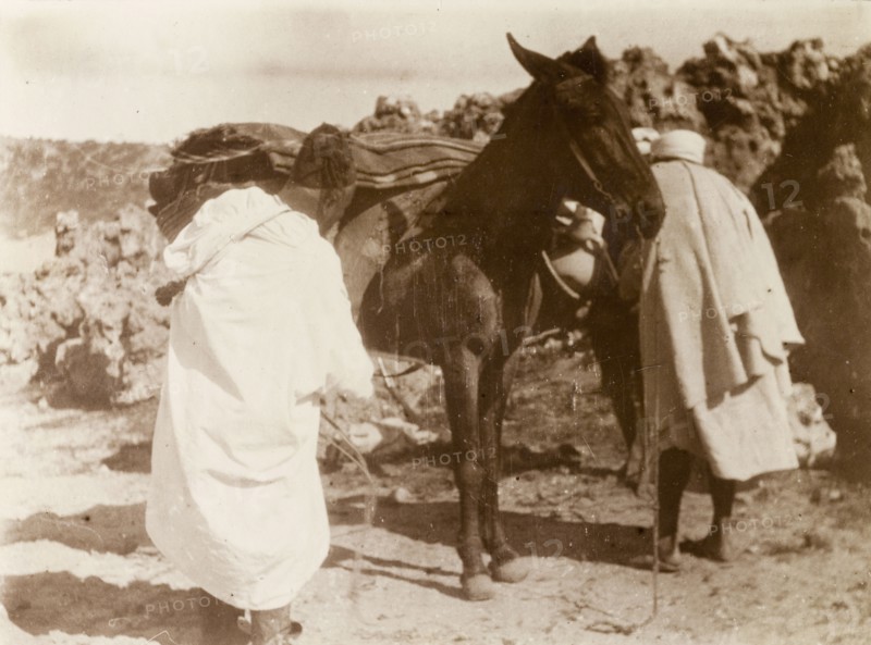 Loading up a mule, Morocco. Two Moroccan men load up their mule with blankets and baskets at a rocky outcrop in the desert. Morocco, 1898. Morocco, Northern Africa, Africa.