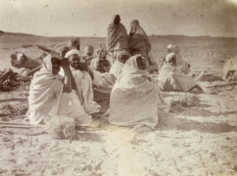 Relaxing after a day's work. A group of Arabic men relax, wrapped in their long white robes, after a hard day's work in the desert. The bundles of string around their feet suggest they may be rope makers. Morocco, 1898. Morocco, Northern Africa, Africa.