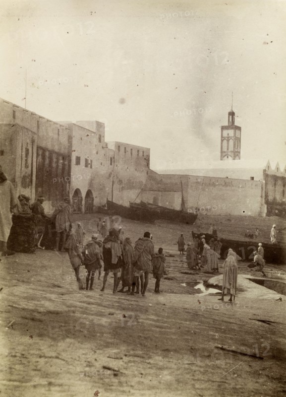 Harbourside market place, Safi. Morrocan people mill about at a market place near the harbour in Safi. Fishing boats can be seen moored on the harbourside. Safi, Morocco, 1898. Safi, Safi, Morocco, Northern Africa, Africa.