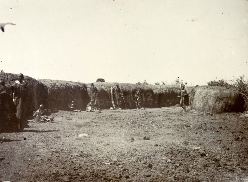 Outside a Maasai village. A group of Maasai are pictured outside the protective mud wall of their village. British East Africa (Kenya), 1906. Kenya, Eastern Africa, Africa.