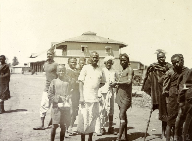 Kenyan men at the station. Local Kenyan men and boys gather for the camera outside a railway station. They may be part of Frederick Stanbury's safari servant entourage who accompanied him on his trip to the Lake Baringo area. Nairobi, British East Africa (Kenya), 1906. Nairobi, Nairobi Area, Kenya, Eastern Africa, Africa.
