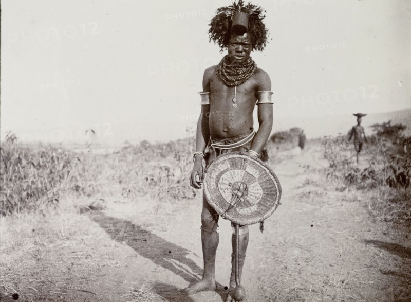 Medicine man, Kenya. Full-length portrait of a man identified in the original caption as a 'witch doctor'. Wearing a headdress and a heavily beaded necklace, he stands proudly holding a wickerwork shield. Near Lake Victoria, British East Africa (Kenya), 1906., Nyanza, Kenya, Eastern Africa, Africa.