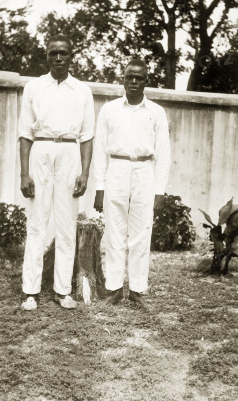Domestic servants in a garden. Portrait of two male domestic servants, 'Joe' a cook and 'Sam' a steward, in a garden. Both men wear white shirts and trousers. Badagry, Nigeria, circa 1928. Badagry, Lagos, Nigeria, Western Africa, Africa.