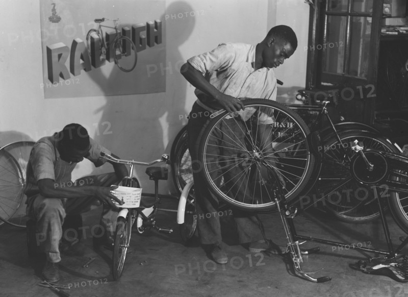 Kassam Kanji's workshop'. Two men at work repairing bicycles of all sizes in a workshop identified as 'Kassam Kanji's'. Kenya, 22 November 1952. Kenya, Eastern Africa, Africa.