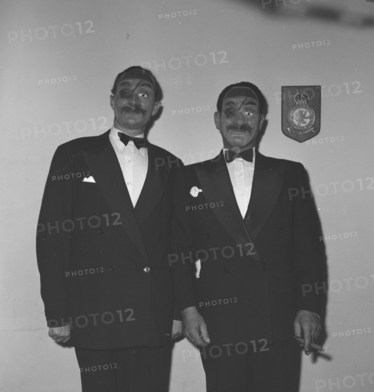 Eric Mathers and Cecil'. Two suited men identified as 'Eric Mathers and Cecil' pose for the camera wearing identical fancy dress masks at the Archer's New Year's Party. Kenya, 31 December 1952. Kenya, Eastern Africa, Africa.
