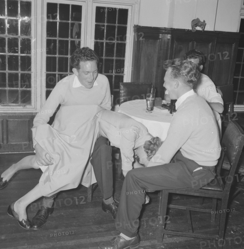 Jazz Ball antics. Three young men in casual dress joke together over the apparently accidental manouevre of a young woman who has fallen across one of their laps at a Jazz Ball. She shares the joke. Kenya, 21 September 1957. Kenya, Eastern Africa, Africa.