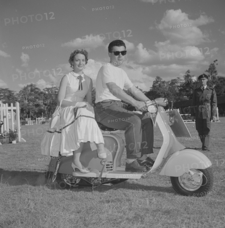 Couple on a scooter. A young couple in typical 1950s Western dress sit on a scooter in a vehicle parade at the Royal Show. Kenya, 25 September 1957. Kenya, Eastern Africa, Africa.