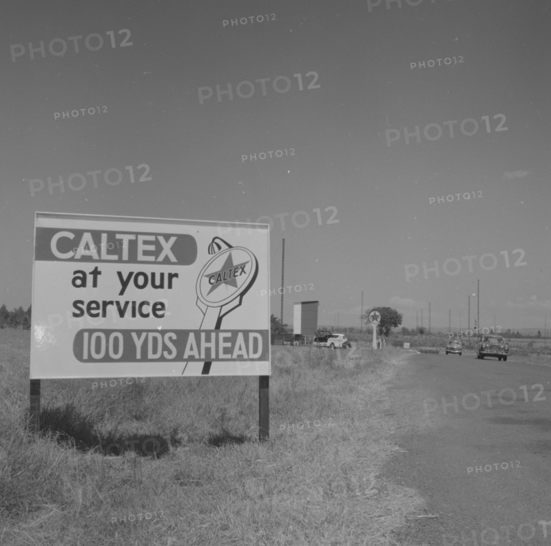 100 yards ahead'. A roadside sign indicates a Caltex Service Service approaching '100 yards ahead'. Kenya, 25 September 1957. Kenya, Eastern Africa, Africa.