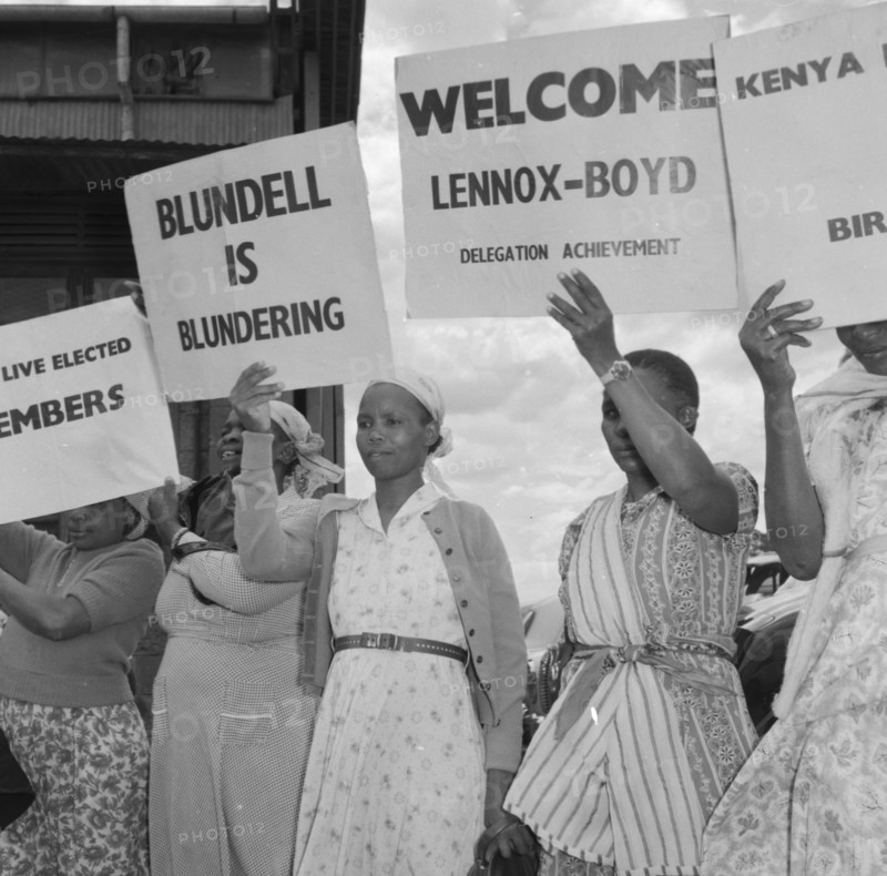 Female Kenyan demonstrators. Several Kenyan women involved in a peaceful demonstration at an airport, hold up placards on the arrival of politican Alan Tindal Lennox-Boyd. Amongst these are two that read: 'Blundell is Blundering' and 'Welcome Lennox-Boyd, Delegation Achievement'. Kenya, 11 October 1957. Kenya, Eastern Africa, Africa.