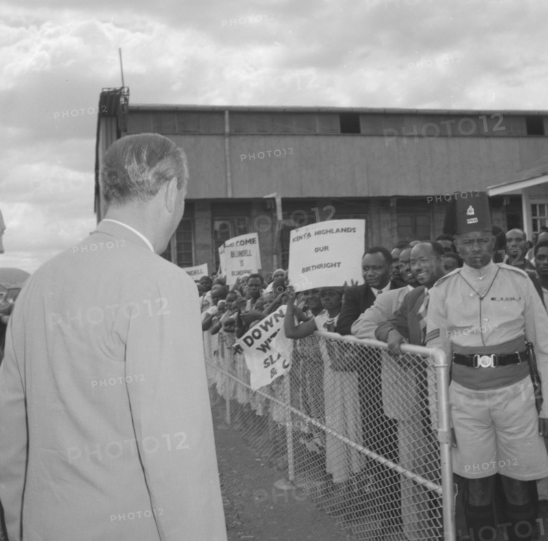 Lennox-Boyd faces demonstrators. Alan Tindal Lennox-Boyd (1904-1983) approaches a peaceful crowd of Kenyan demonstrators, held back by askaris (soldiers) behind a barrier. Amongst the placards on display are two that read: 'Kenya Highlands, Our Birthright' and 'Blundell is Blundering'. Kenya, 11 October 1957. Kenya, Eastern Africa, Africa.