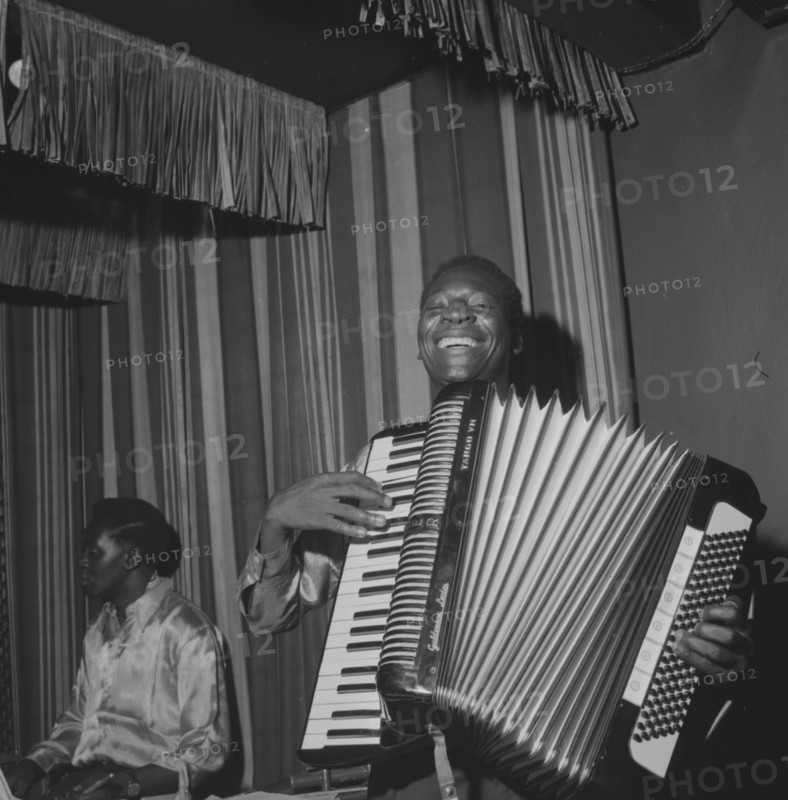 Accordion player. An African musician smiles broadly as he squeezes an accordion during a performance at the Equator Club. Nairobi, Kenya, 19 October 1957. Limuru, Central (Kenya), Kenya, Eastern Africa, Africa.