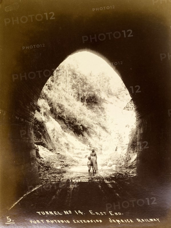 Inside railway tunnel 'No. 14'. View from inside railway tunnel 'No. 14', looking out towards a woman and child who stand at the east entrance. The tunnel is shown before the construction of the railway track that would later run beneath it as part of the Port Antonio extension line. Portland, Jamaica, circa 1895., Portland, Jamaica, Caribbean, North America .