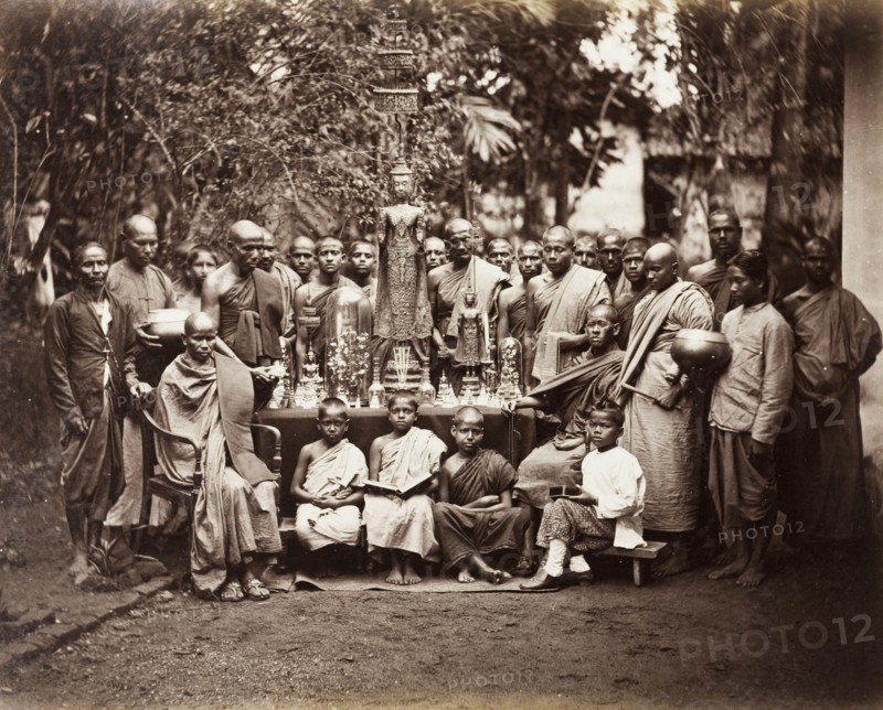 Buddhist monks with religious icons. A group of Buddhist monks stand around a table laden with religious icons including metal statues, figurines and vessels. Two robed monks are seated on either side of the table whilst four young boys squat on stools at the front of the group. Ceylon (Sri Lanka), circa 1875. Kandy, Central (Sri Lanka), Sri Lanka, Southern Asia, Asia.