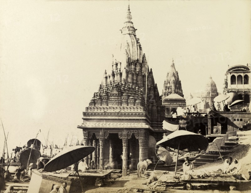 Scindia Ghat and Manikarnika Ghat. The temples of Scindia Ghat and Manikarnika Ghat, located on the banks of the River Ganges. Pilgrimage priests can be seen, seated beneath large umbrellas in the foreground. Benares, North Western Provinces (Varanasi, Uttar Pradesh), India, circa 1875. Varanasi, Uttar Pradesh, India, Southern Asia, Asia.