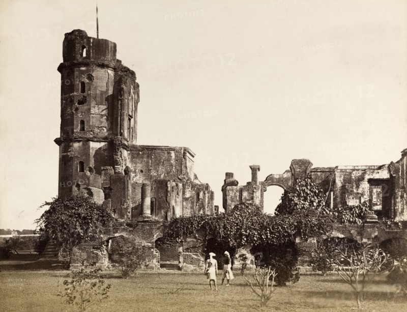 Ruins of the British Residency. The British Residency at Lucknow, ruined during the Indian Mutiny of 1857-8. The ruins are partially overgrown with climbing plants and an empty flagstaff protrudes from a tower. In the foreground, two Indian gardeners walk across tended grounds. Lucknow, North Western Provinces (Uttar Pradesh), India, circa 1880. Lucknow, Uttar Pradesh, India, Southern Asia, Asia.