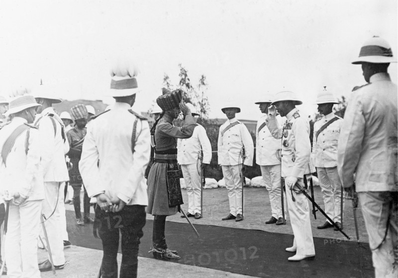 King George V salutes an officer. An Indian officer is presented to King George V (r.1910-36) on a red carpet laid out in front of Government House. The royal couple stopped at Aden during their outward journey to India for the Coronation Durbar at Delhi. Aden,Yemen, circa 27 November 1911. Aden, Adan, Yemen, Middle East, Asia.
