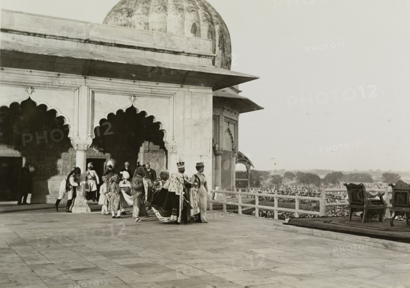 The royal couple at the Delhi Fort. King George V (r.1910-36) and Queen Mary emerge before crowds onto a throned balcony at the Delhi Fort. Pictured the day after the Coronation Durbar, they are dressed in their coronation robes and crowns, and are accompanied by ten Indian pages. New Delhi, India, 13 December 1911. India, Southern Asia, Asia.