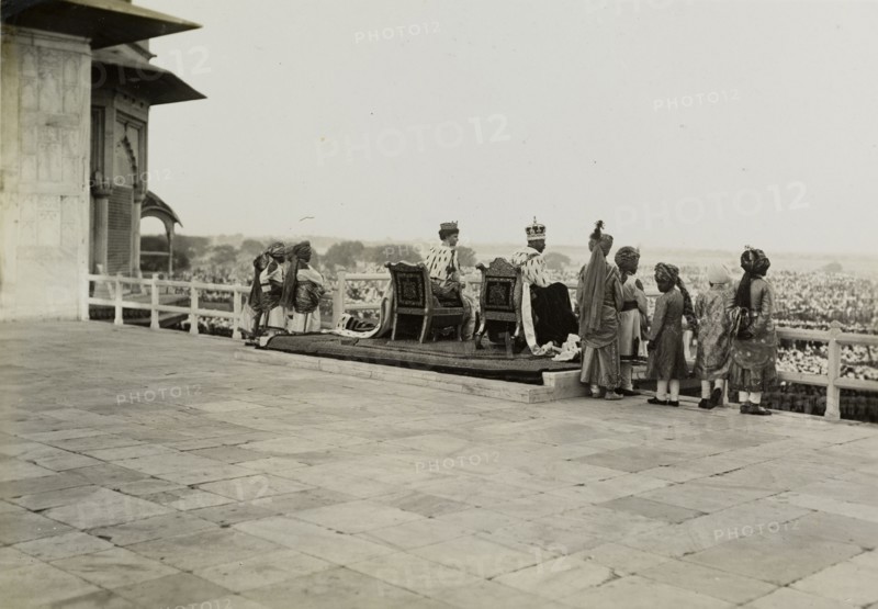 The royal couple at the Delhi Fort. King George V (r.1910-36) and Queen Mary appear before crowds from a throned balcony at the Delhi Fort. Pictured the day after the Coronation Durbar, they are dressed in their coronation robes and crowns, and are accompanied by ten Indian pages. Delhi, India, 13 December 1911. Delhi, Delhi, India, Southern Asia, Asia.