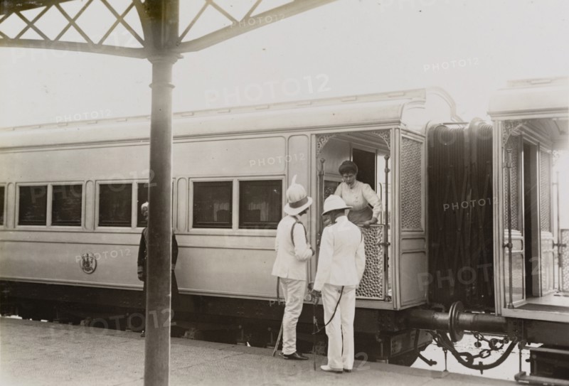 Queen Mary leans from the royal train. Queen Mary leans from the royal train to talk with Sir Derek Keppel and Sir Charles Cust. The train stands at an Indian railway station en route from Kolkata to Mumbai. India, circa 4 January 1912. India, Southern Asia, Asia.