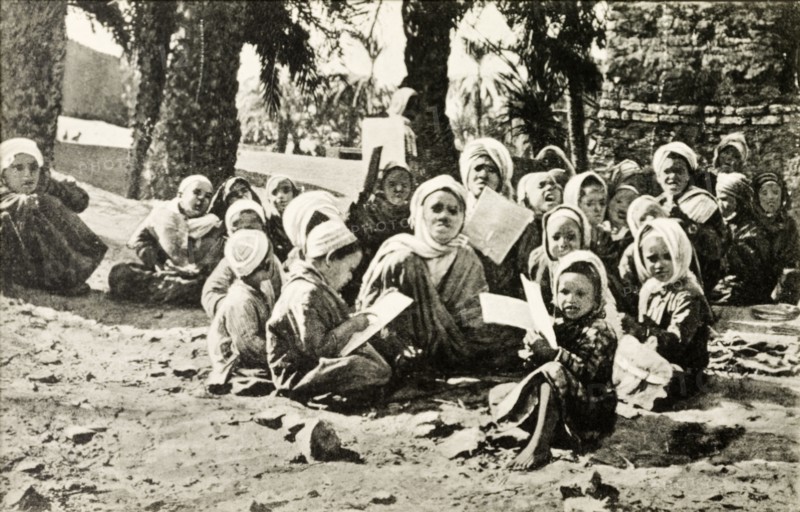 Outdoors school, Egypt. A group of young children sit cross-legged on a patch of desert sand as they take their lessons at an outdoors school. Egypt, circa 1925. Egypt, Northern Africa, Africa.