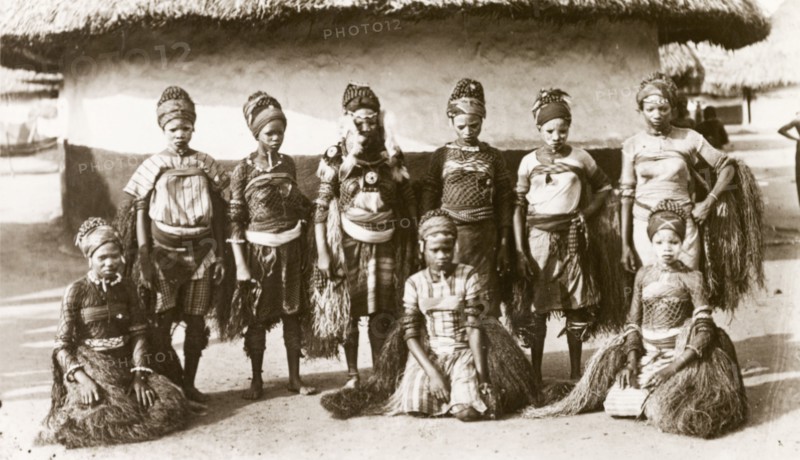 Sierra Leone dancers. Nine young women dressed in traditional dance costume pose for the camera wearing grass skirts, headscarves and face paint. Sierra Leone, circa 1910. Sierra Leone, Western Africa, Africa.