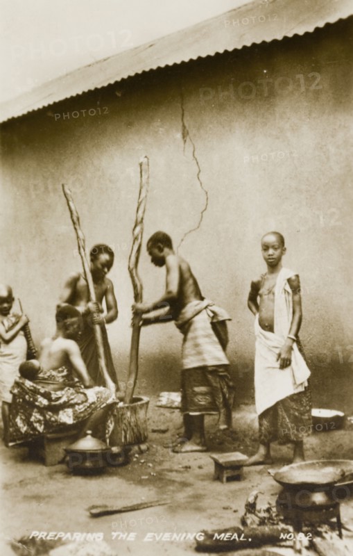 Pounding fufu. Two women prepare fufu, a staple food of West and Central Africa, by pounding the starchy mixture using a large pestle and mortar. Gold Coast (Ghana), circa 1910. Ghana, Western Africa, Africa.