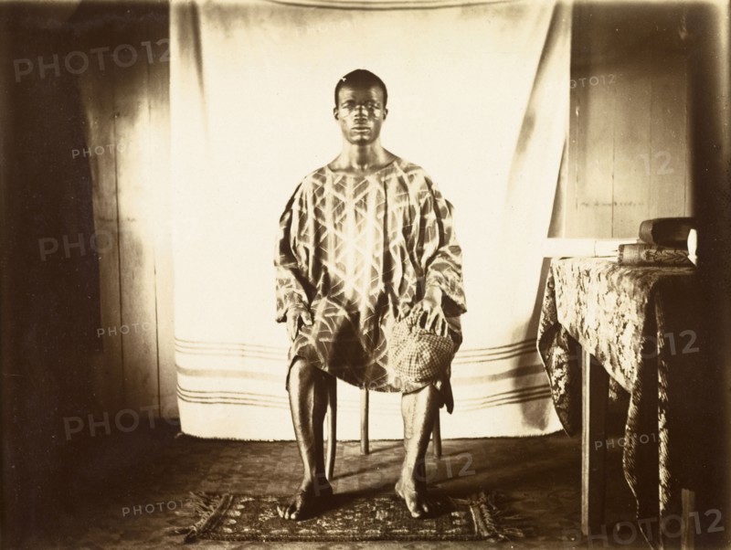 Young man from Bioko. Portrait of a traditionally dressed young man from Bioko, posed seated against a makeshift backdrop. Bioko, Equatorial Guinea, circa 1930., Bioko Norte, Equatorial Guinea, Central Africa, Africa.