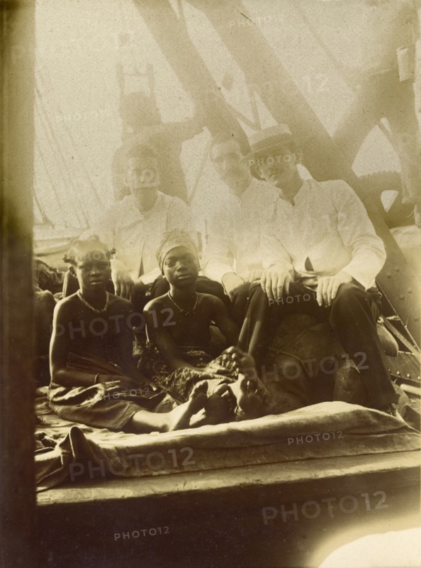 European men, African girls. Three European men accompany two African girls on what appears to be the deck of a ship. This photograph is one of around 70 images compiled by a British Primitive Methodist missionary documenting life on the island of Bioko during the 1930s. Location unknown, circa 1930.