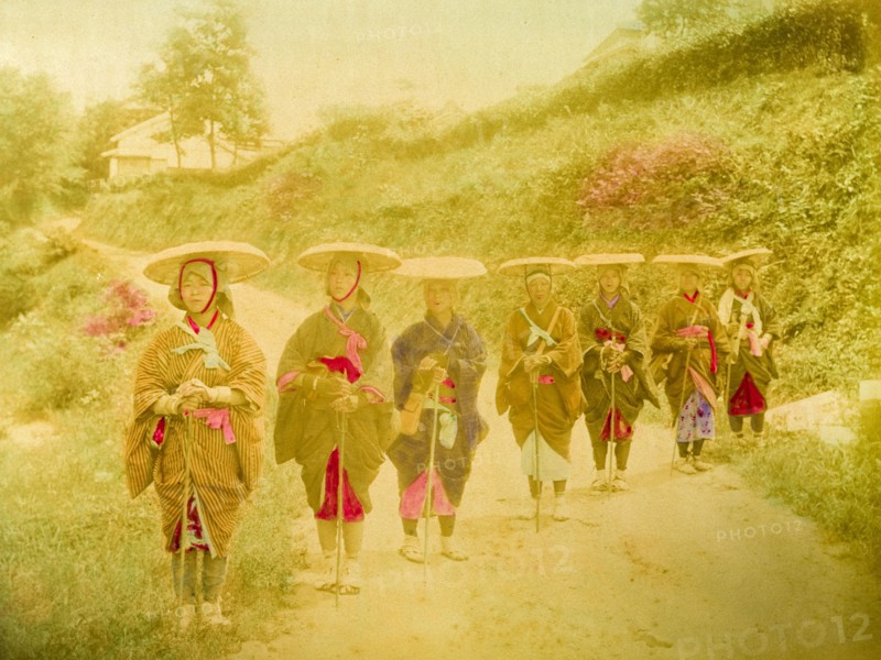Japanese women. Seven Japanese women stand in line on a rural road. Traditionally dressed in kimonos, they wear flat straw hats secured with chin straps and rags wrapped around their feet. Japan, circa 1910. Japan, Eastern Asia, Asia.
