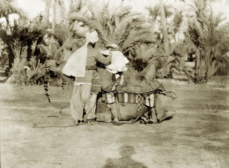 Margaret Lawrence prepares to ride a camel. Margaret Lawrence (b.1904), the daughter of Phyllis and Sir Henry Staveley Lawrence (Collector of Karachi), clambers up onto the back of a saddled camel with the aid of an Indian servant. Karachi, India (Pakistan), circa 1910. Karachi, Sindh, Pakistan, Southern Asia, Asia.