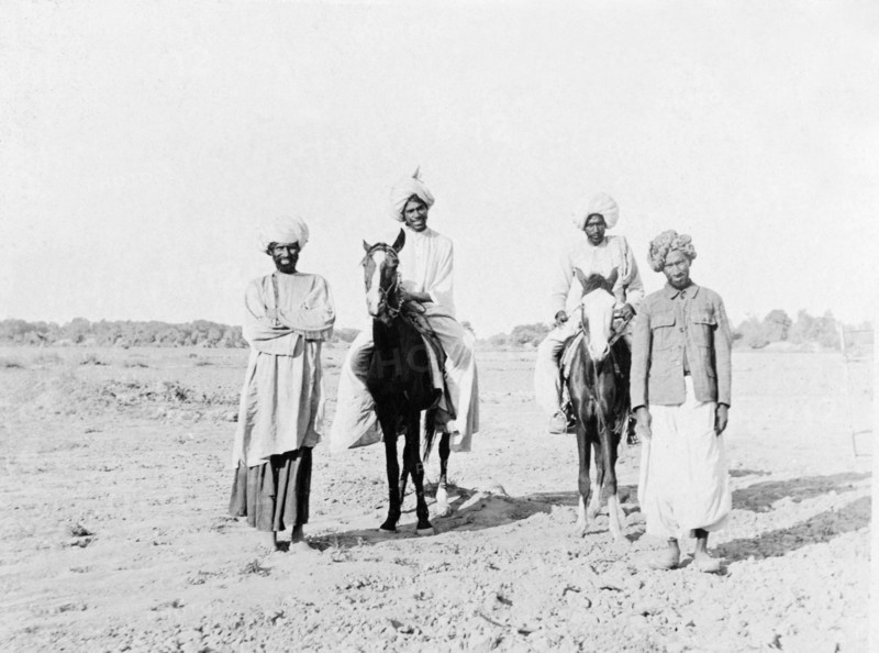 Portrait of four Indian men with horses. Portrait of four men in traditional Indian dress, two of whom sit astride saddled horses. Sukkur, Sind, India (Sindh, Pakistan), circa 1908. Sukkur, Sindh, Pakistan, Southern Asia, Asia.