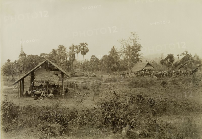 British Army camp at Sin-gon. British Army soldiers take at rest at Sin-gon. The company was involved in a campaign to suppress Burmese rebels in Wuntho State (Sagaing Division). Several of the men relax inside an open-walled dwelling, whilst a herd of unsaddled horses gathers to graze in the distance. Sin-gon, Burma (Myanmar), 1891. Sin-gon, Sagaing, Burma (Myanmar), South East Asia, Asia.