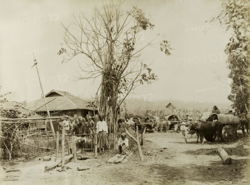 Soldiers visit a Burmese village. British and Indian soldiers visit a Burmese village. Possibly a mix of British Army and Military Police officers, the men were involved in a campaign to suppress Burmese rebels in Wuntho State (Sagaing Division). A local man works a wooden lathe, whilst others sit inside carts pulled by bullocks. Youngma, Burma (Myanmar), 1891. Youngma, Sagaing, Burma (Myanmar), South East Asia, Asia.