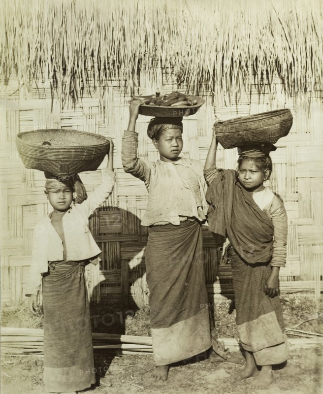 Three Burmese girls at Wuntho. Three young Burmese girls pose outside a thatched dwelling, balancing baskets of ripe bananas on their heads. Wuntho, Burma (Myanmar), circa 1891. Wuntho, Sagaing, Burma (Myanmar), South East Asia, Asia.